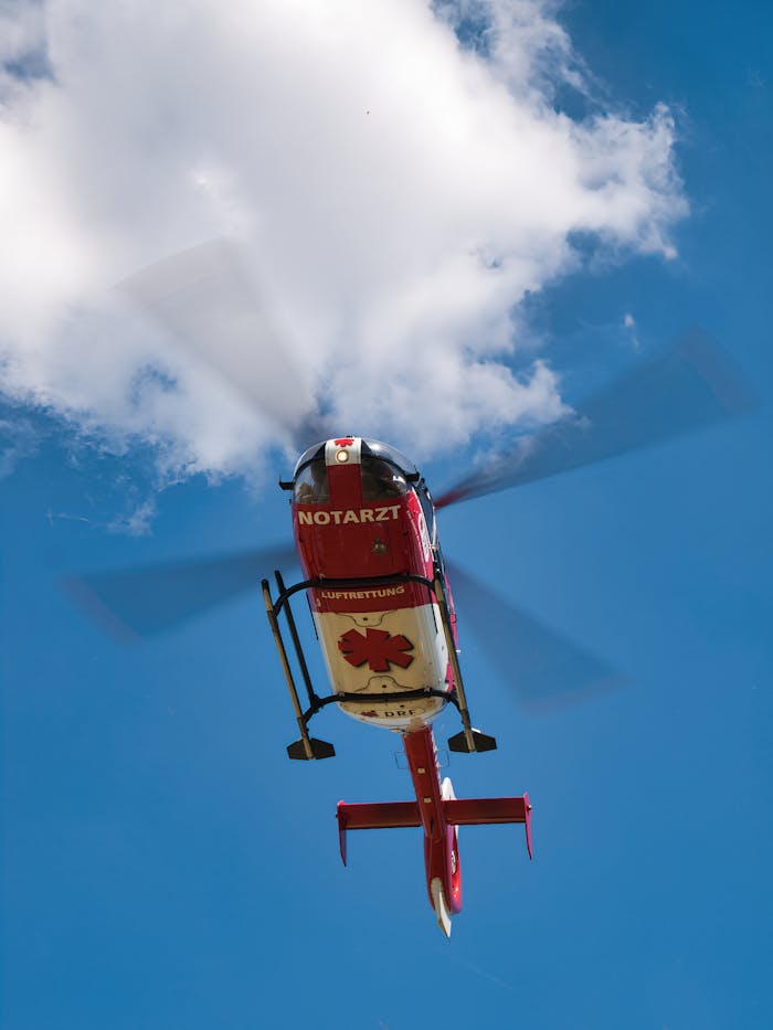 Red rescue helicopter flying under a cloudy sky, showcasing emergency medical service in action.